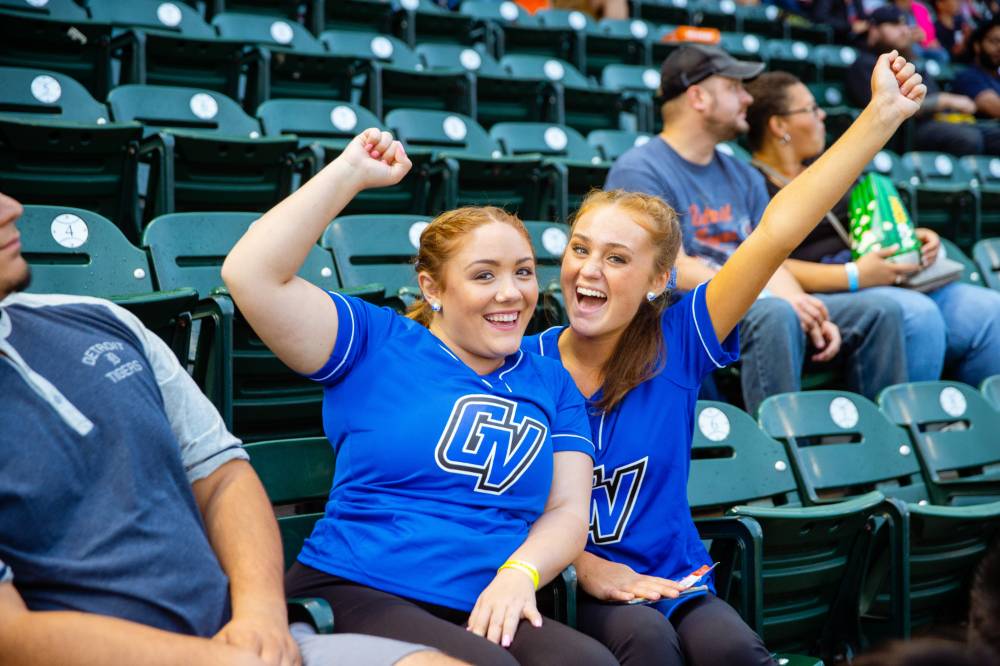 two girls in gvsu shirts are throwing their fists in the air rooting for the tigers